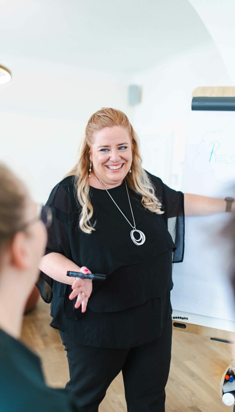 Die Beraterin und Supervisorin Sandra Kremmel steht bei einem Workshop vor einen Flipchart und einigen Teilnehmerinnen