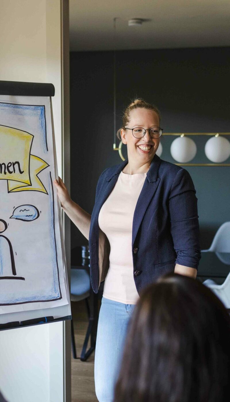 Die Beraterin und Supervisorin Tanja Pitzer steht bei einem Workshop vor einen Flipchart und einigen Teilnehmerinnen